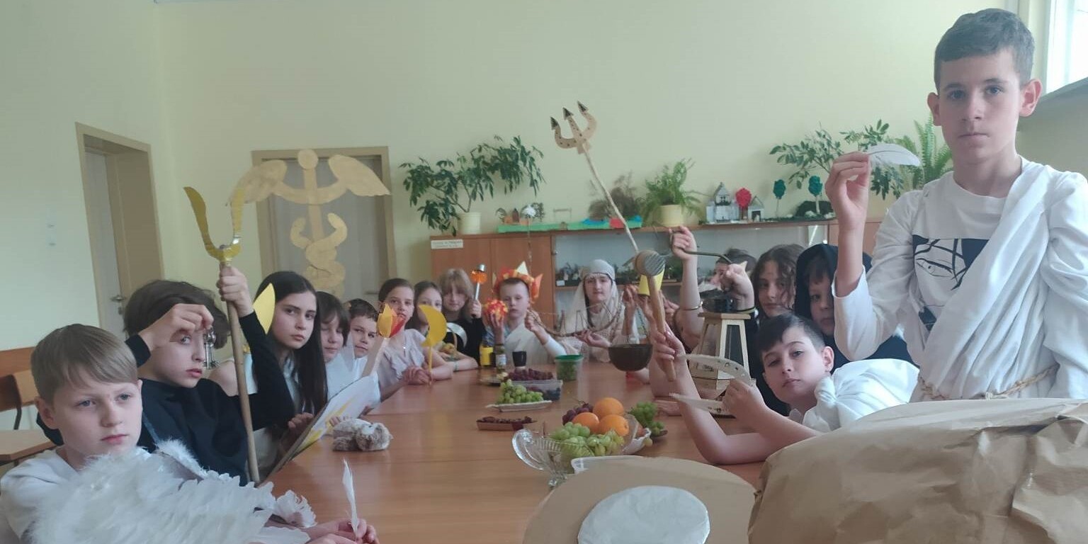 uczniowie przebrani za greckich bogów siedzą przy wspólnym stole