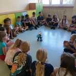 Dzieci siedząc w okręgu obserwują robota.