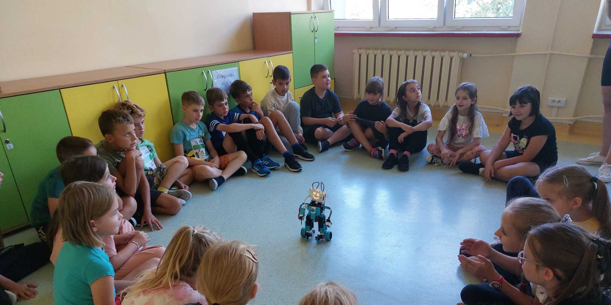 Dzieci siedząc w okręgu obserwują robota.