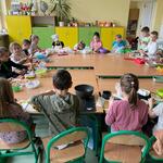 Uczniowie siedząc przy wspólnym stole przygotowują sałatkę owocową.