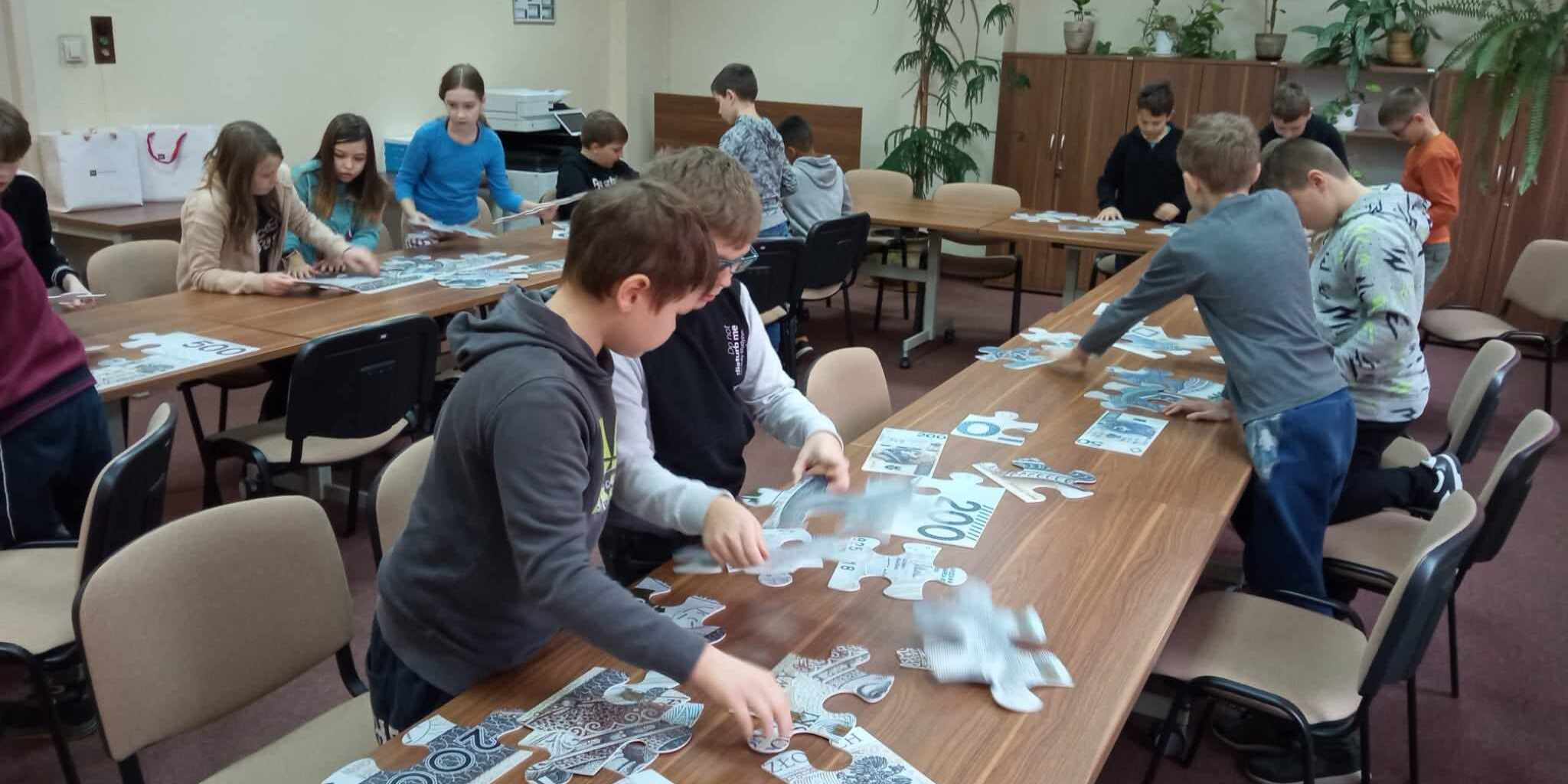Uczniowie biorą udział w zajęciach. Układają duże puzzle banknotów