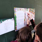 Uczniowie przy tablicy czytają list od Mikołaja. Szukają swoich imion na liście.