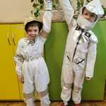 Chłopcy w strojach astronauty podnoszą ręce do góry, jakby szykowali się do lotu na Księżyc.
