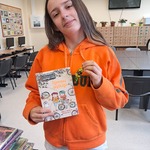 Uczennica pozuje do zdjęcia z książką i czekoladowymi cukierkami.