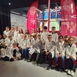 Uczniowie pozują do zdjęcia. Są ubrani w białe fartuchy i okulary ochronne.