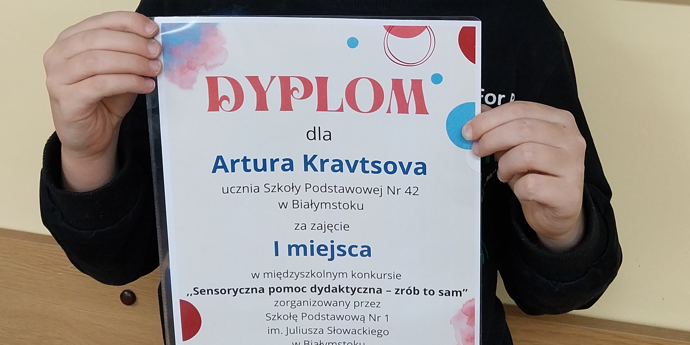 Uczeń pozuje do zdjęcia z dyplomem.