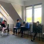 Uczniie podczas warsztatów. Siedzą w kole. Wypełniają karty pracy.