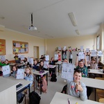 uczniowie w klasie podnoszą do góry wykonane karty pracy