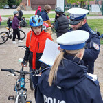 Uczeń przytrzymuje rower. Obok niego stoi policjant i sprawdza swoje notatki.