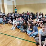 Uczniowie siedzą na podłodze. Słuchają lekcji.