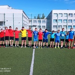 Uczniowie pozują do zdjęcia na boisku szkolnym. Są ubrani w stroje sportowe