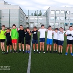 Uczniowie pozują do zdjęcia na boisku szkolnym. Są ubrani w stroje sportowe