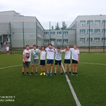 Uczniowie pozują do zdjęcia na boisku szkolnym. Są ubrani w stroje sportowe