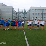 Uczniowie pozują do zdjęcia na boisku szkolnym. Są ubrani w stroje sportowe 