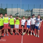 Uczniowie pozują do zdjęcia na boisku szkolnym. Są ubrani w stroje sportowe