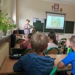 Ucznniowie siedzą w ławkach w sali. Nauczyciel czyta im książkę. Wyświetla treści z rzutnika na tablicę