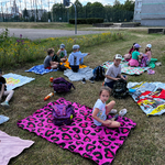 Uczniowie są na pikniku. Siedzą na kocach na trawie. Grają w gry planszowe i karciane. 