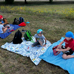 Uczniowie są na pikniku. Siedzą na kocach na trawie. Grają w gry planszowe i karciane. 