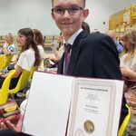 Uczeń pozuje do zdjęcia z medalem i dyplomem