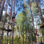 Uczniowie pokonują trasę w parku linowym. Są ubrani w kaski i uprzęże do wspinaczki