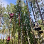 Uczniowie pokonują trasę w parku linowym. Są ubrani w kaski i uprzęże do wspinaczki