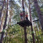 Uczniowie pokonują trasę w parku linowym. Są ubrani w kaski i uprzęże do wspinaczki