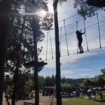 Uczniowie pokonują trasę w parku linowym. Są ubrani w kaski i uprzęże do wspinaczki