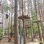 Uczniowie pokonują trasę w parku linowym. Są ubrani w kaski i uprzęże do wspinaczki