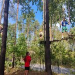 Uczniowie pokonują trasę w parku linowym. Są ubrani w kaski i uprzęże do wspinaczki