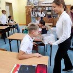 Uczniowie siedzą w ławkach. Jeden uczeń z ławki zagląda do pudełka