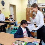 Uczniowie siedzą w ławkach. Jeden uczeń zagląda do pudełka