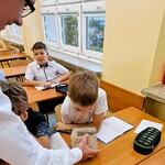 Uczniowie siedzą w ławkach. Jeden uczeń z ławki zagląda do pudełka