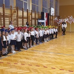Uczniowie pozują do zdjęcia. Wszyscy są ubrani na galowo oraz mają na głowach kolorowe birety.