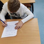 Uczeń siedzi przy ławce. Pisze dyktando