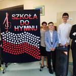 Uczniowie pozują do zdjęcia przy tablicy z napisem Szkoła do hymnu
