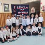 Uczniowie pozują do zdjęcia przy tablicy z napisem Szkoła do hymnu
