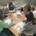 Uczniowie siedzą przy kwadratowych stolikach w grupach. Robią notatki wizualne