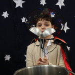 Chłopiec w przebraniu czarnoksiężnika trzyma w rękach dwie chochle. 
