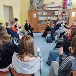 Uczniowie siedzą na krzesłach w kole. Trzymają kciuki w górze.