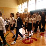 Uczniowie tańczą poloneza na sali gimnastycznej podczas uroczystej akademii