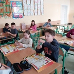 Uczniowie siedzą w ławkach. Wycinają z szablonu kształty