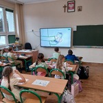 Uczniowie siedzą w ławkach. Oglądają film o numerach alarmowych.