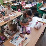 Uczniowie siedzą w ławkach. Kolorują plakaty.