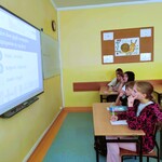 Uczniowie siedzą w ławkach. Patrzą na tablicę i rozwiązują quiz.