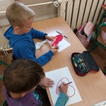 Uczniowie siedzą przy ławkach. Wycinają kształt serca.