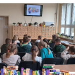 Dzieci siedzą w bibliotece i słuchają czytanej bajki