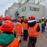 Uczniowie zwiedzają Zakład Unieszkodliwiania Odpadów. Są ubrani w odblaskowe kamizelki i kaski.