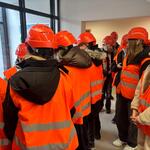 Uczniowie zwiedzają Zakład Unieszkodliwiania Odpadów. Są ubrani w odblaskowe kamizelki i kaski.