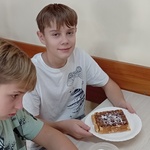 Uczniowie pozują do zdjęcia. Na talerzu leży gofr.