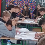 Uczniowie siedzą w ławkach. Rozwiązują zadania